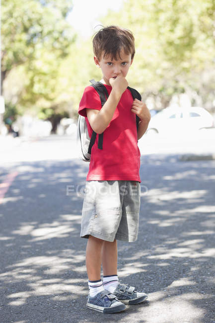 Portrait de mignon petit garçon debout avec le doigt dans la bouche à l'extérieur — Photo de stock