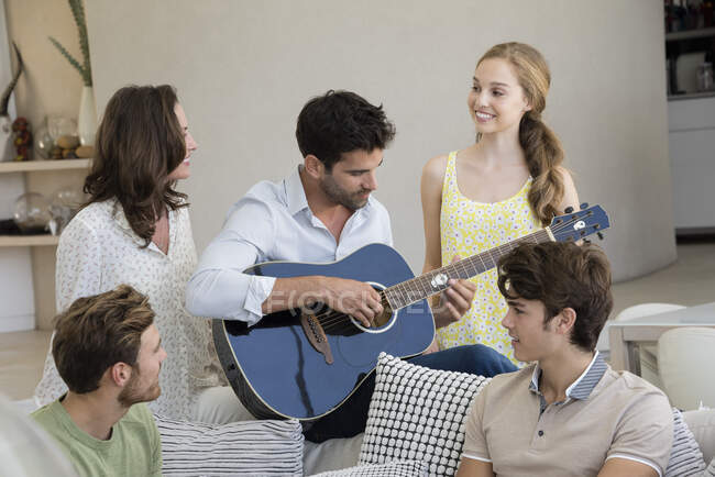 Glücklicher Mann, der mit seinen Freunden um sich herum eine Gitarre spielt — Stockfoto