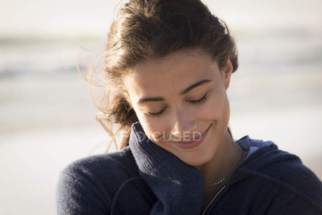 Primer plano de la joven encantadora mujer con los ojos cerrados sonriendo en la playa - foto de stock