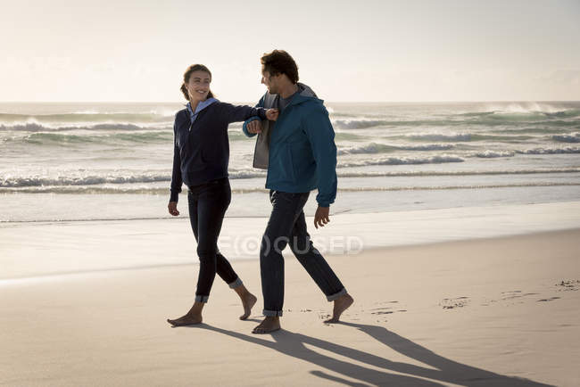 Feliz joven pareja alegre caminando en la playa en otoño - foto de stock