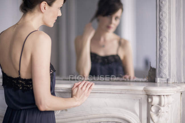 Reflexão da mulher elegante em vestido de noite preto olhando para o espelho — Fotografia de Stock