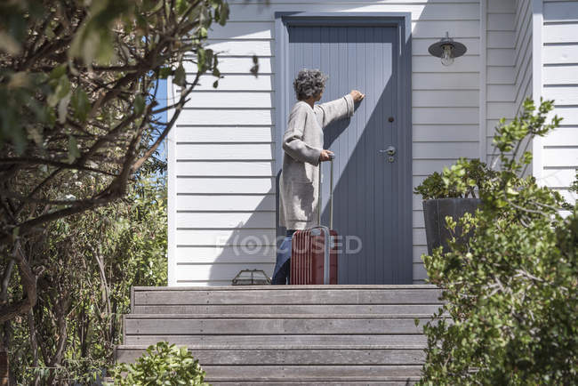 Woman with suitcase knocking on door of countryside house — Stock Photo