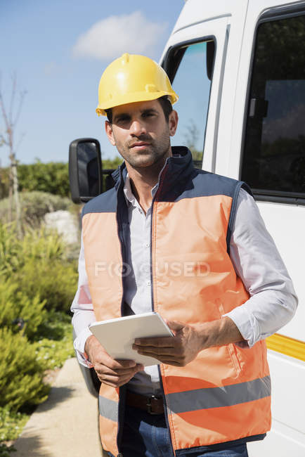 Male engineer with digital tablet standing at van and looking at camera — Stock Photo