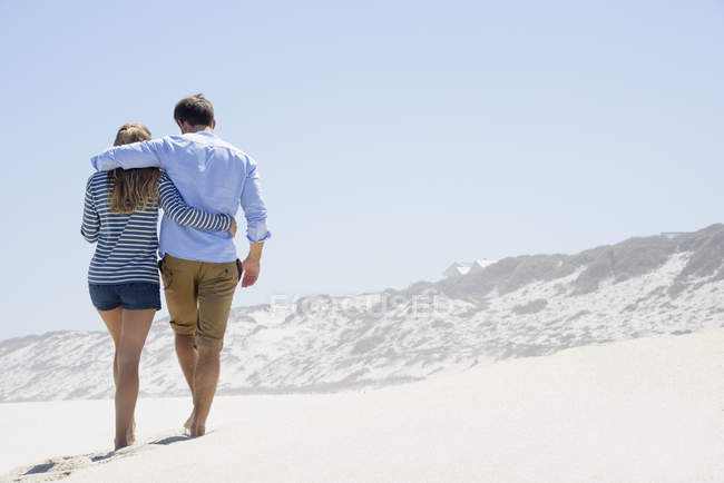 Вид сзади на романтическую пару, гуляющую по песчаному пляжу — стоковое фото
