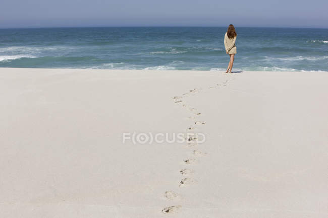 Visão traseira da mulher relaxada em pé na praia de areia — Fotografia de Stock