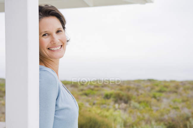 Retrato de mujer sonriente apoyada en el poste en la naturaleza - foto de stock