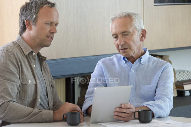 Senior man sharing digital tablet with financial advisor at home — Stock Photo