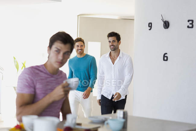 Jeune homme prenant un café à la maison avec des amis marchant sur le fond — Photo de stock