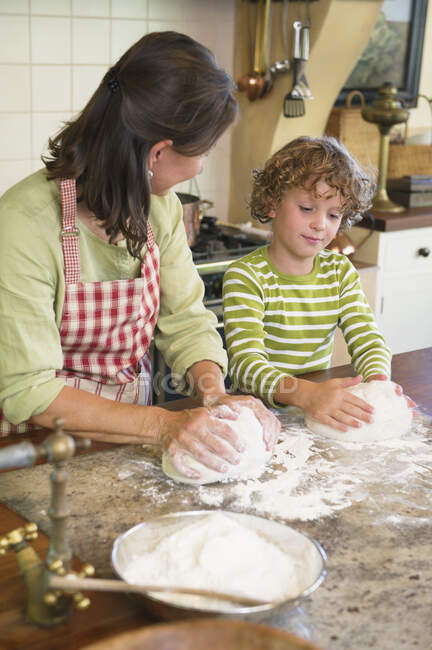 Grand-mère et petit garçon pétrissant la pâte à la cuisine — Photo de stock