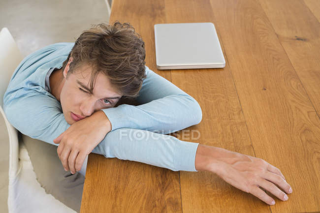 Молодий чоловік спирається на дерев'яний стіл з ноутбуком — стокове фото