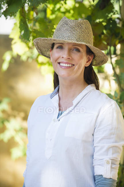 Портрет усміхненої зрілої жінки в солом'яному капелюсі в саду — стокове фото