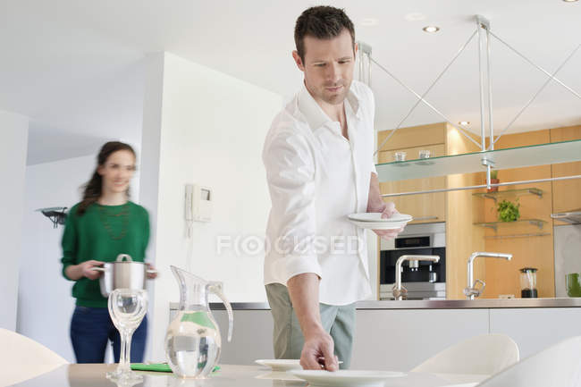 Homem servindo mesa para jantar com esposa no fundo — Fotografia de Stock