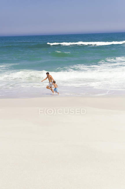 Homem brincalhão brincando com o filho na praia de areia — Fotografia de Stock
