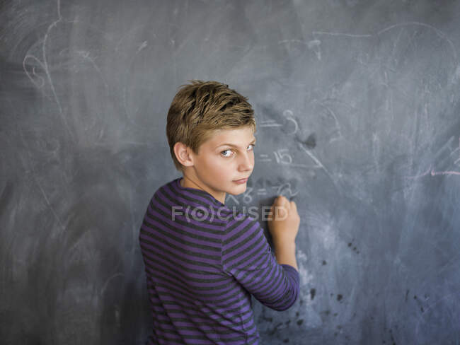Garçon écrit sur un tableau noir dans une salle de classe — Photo de stock