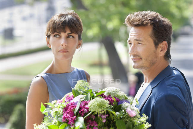 Casal elegante com buquê de flores em pé ao ar livre — Fotografia de Stock