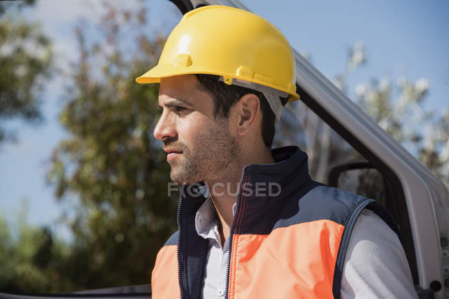 Engenheiro masculino em capacete em pé na van e olhando para longe — Fotografia de Stock