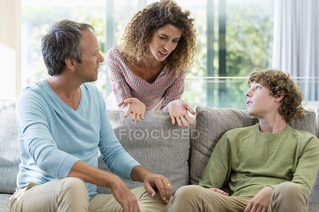 Familia feliz hablando en el sofá en la sala de estar en casa - foto de stock