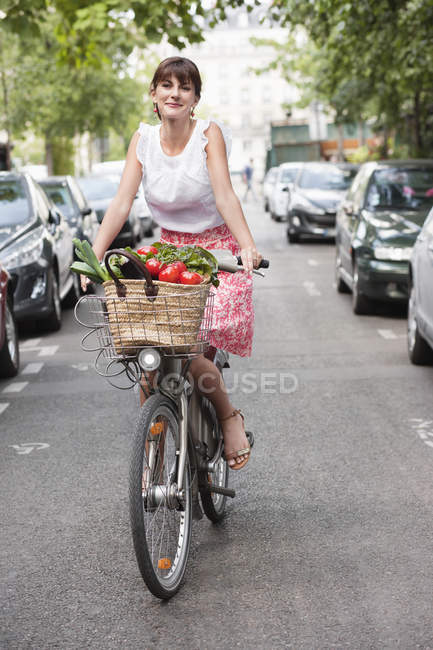 Portrait of smiling woman carrying vegetables while riding bicycle — Stock Photo