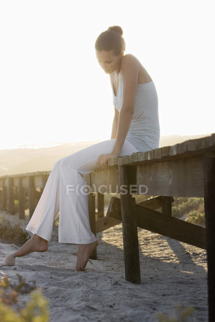 Donna elegante pensierosa seduta su una passerella sulla costa — Foto stock