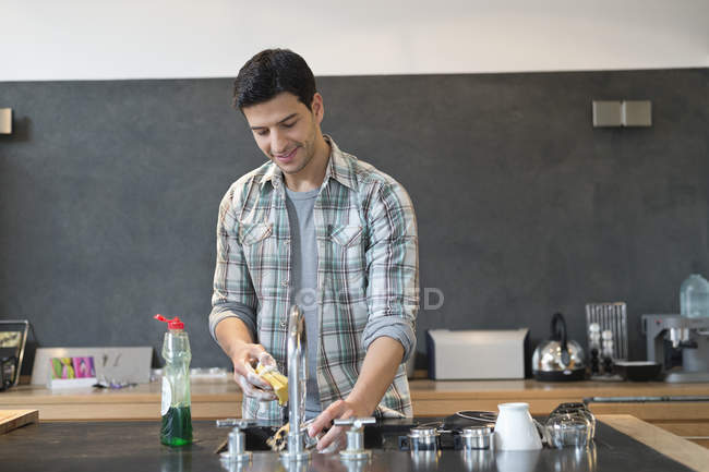 Uomo sorridente che lava i piatti nella cucina moderna — Foto stock