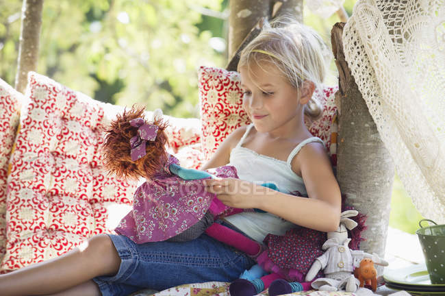 Petite fille tenant des jouets dans la maison des arbres — Photo de stock