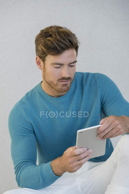 Homem jovem usando tablet digital contra a parede cinza — Fotografia de Stock