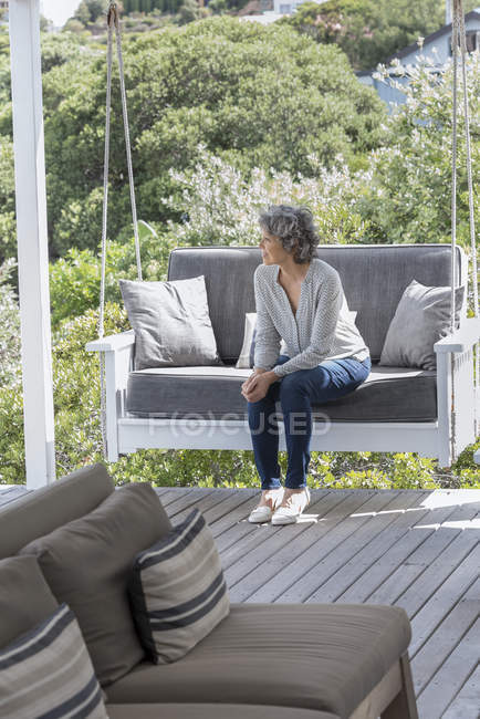Mulher feliz relaxando na cadeira de balanço no alpendre e olhando para longe — Fotografia de Stock