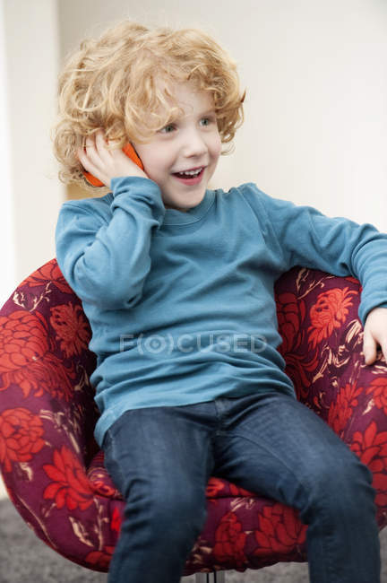 Menino bonito com cabelo loiro falando em um telefone celular em poltrona — Fotografia de Stock
