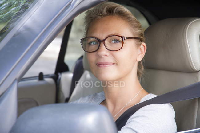 Primo piano della donna sorridente che indossa occhiali da vista alla guida di una macchina — Foto stock