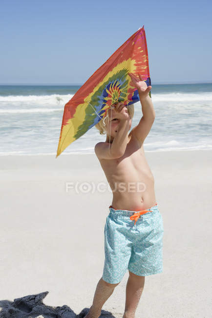 Счастливый мальчик держит змея на песчаном пляже — стоковое фото