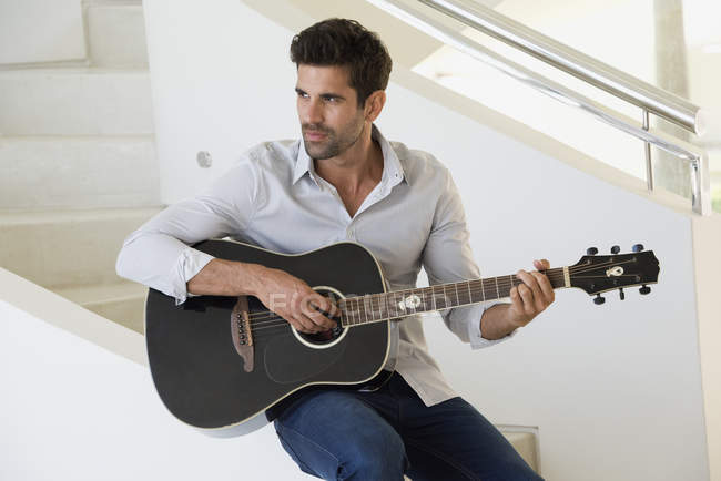 Hombre confiado tocando la guitarra en casa - foto de stock