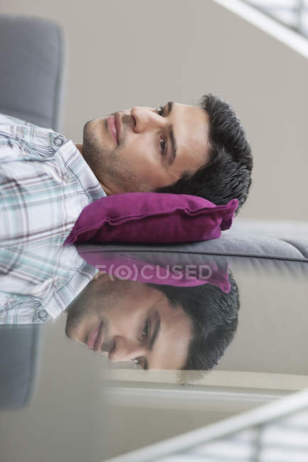 Hombre relajado acostado en el sofá con la reflexión sobre la mesa de cristal - foto de stock