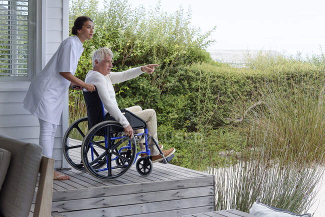 Жіноча медсестра допомагає старшому чоловікові в інвалідному візку на ганку — стокове фото