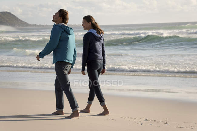 Счастливая босиком молодая пара, гуляющая по пляжу осенью — стоковое фото
