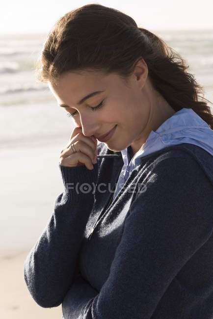 Charming young woman in hoodie standing on beach — Stock Photo