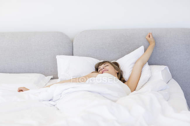 Сонная женщина просыпается и зевает с растяжением в постели — стоковое фото