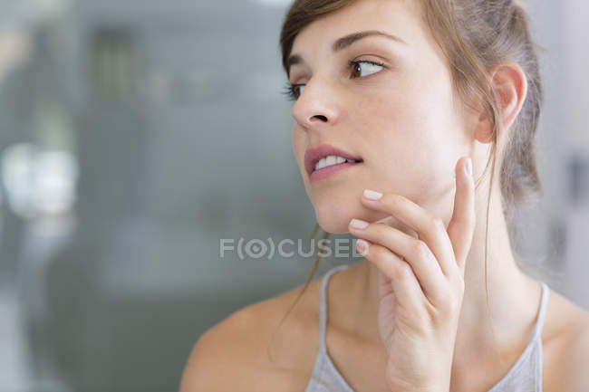 Jeune femme appliquant une crème hydratante sur les joues — Photo de stock