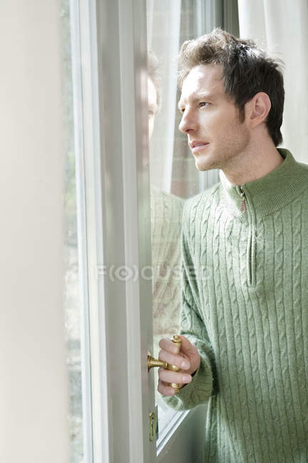 Человек в пуловере смотрит через стекло двери — стоковое фото