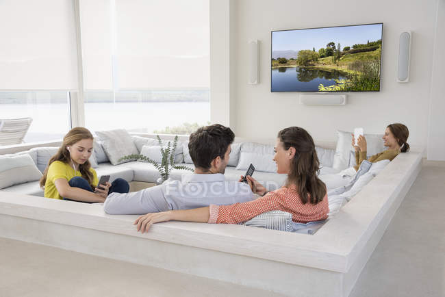 Pareja viendo televisión con hijas ocupadas con gadgets - foto de stock