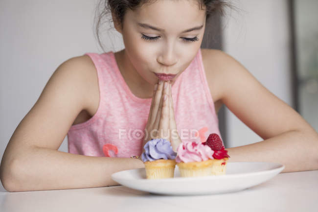 Chica pensativa mirando cupcakes en la mesa - foto de stock