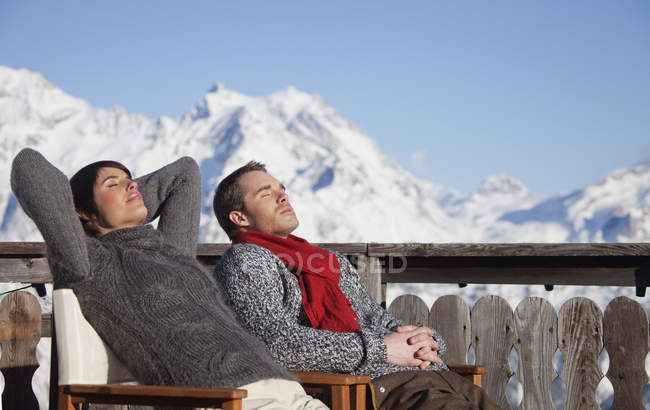 Молода пара насолоджується зимовим сонцем на дерев'яній терасі в горах — стокове фото