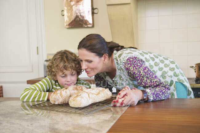 Lindo niño y madre oliendo pan horneado - foto de stock