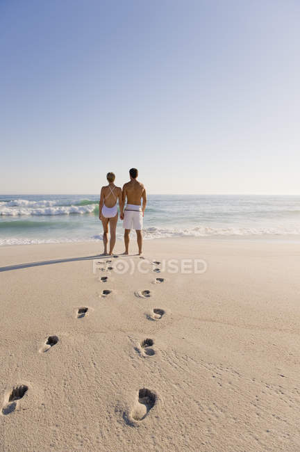 Сліди на піщаний пляж з пара стоячи на фоні і, дивлячись на вид — стокове фото
