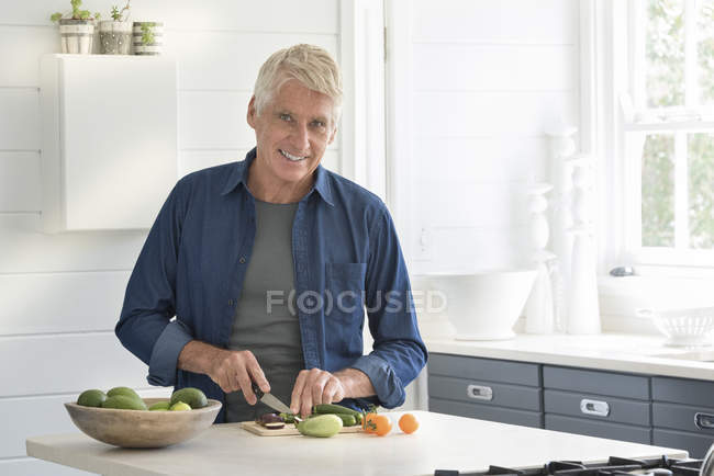 Happy senior man preparing vegetables in kitchen and looking at camera — Stock Photo