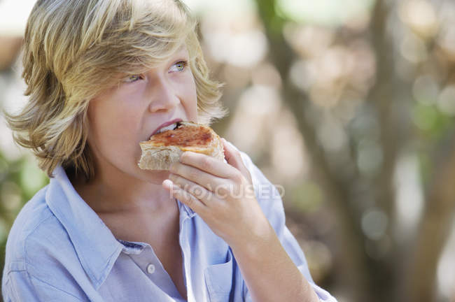 Chico con pelo rubio comer sándwich al aire libre — Stock Photo
