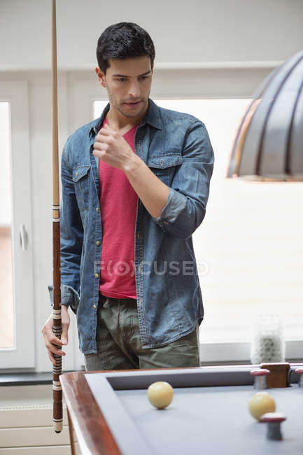 Hombre reflexivo con taco de billar mirando una mesa de billar - foto de stock