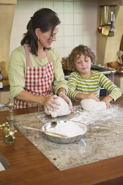 Grand-mère et petit garçon pétrissant la pâte à la cuisine — Photo de stock