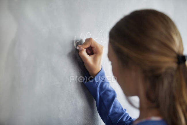 Primer plano de la adolescente escribiendo en pizarra en un aula - foto de stock