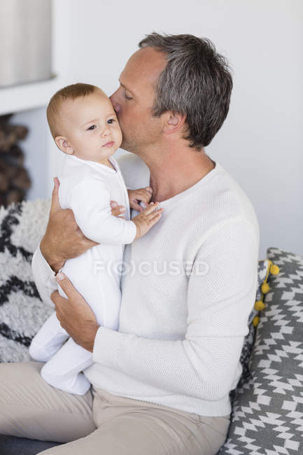Батько цілує милу доньку на дивані у вітальні — стокове фото