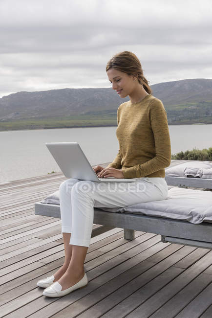 Sorrindo jovem mulher usando laptop na margem do lago — Fotografia de Stock